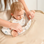 Demonstration of how to attach the long-sleeve bib to the high chair tray. | Démonstration de la fixation du bavoir à manches longues sur le plateau de la chaise haute.