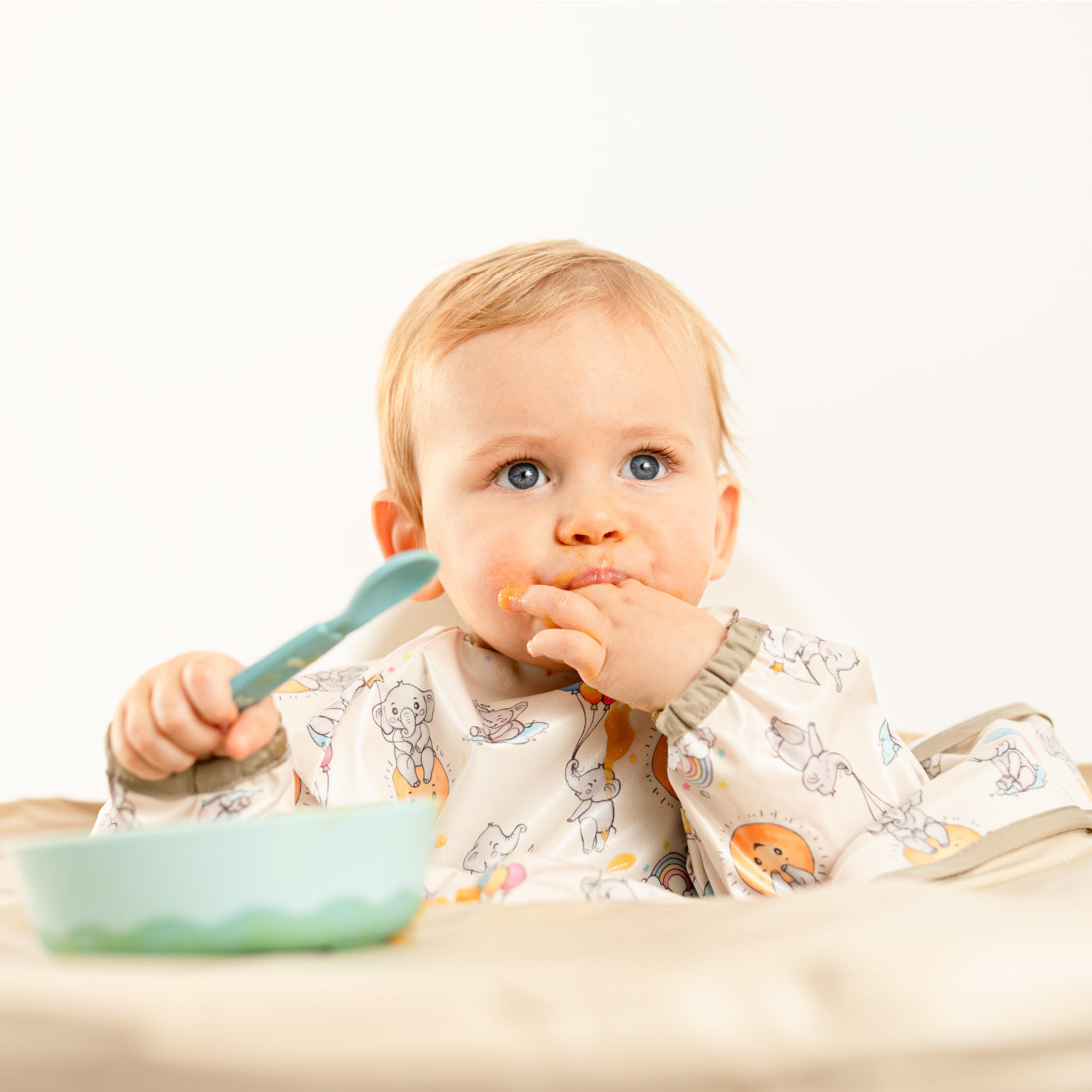 Baby focused on self-feeding with a spoon and Bibatray protection. | Bébé concentré à manger seul avec une cuillère et la protection Bibatray.
