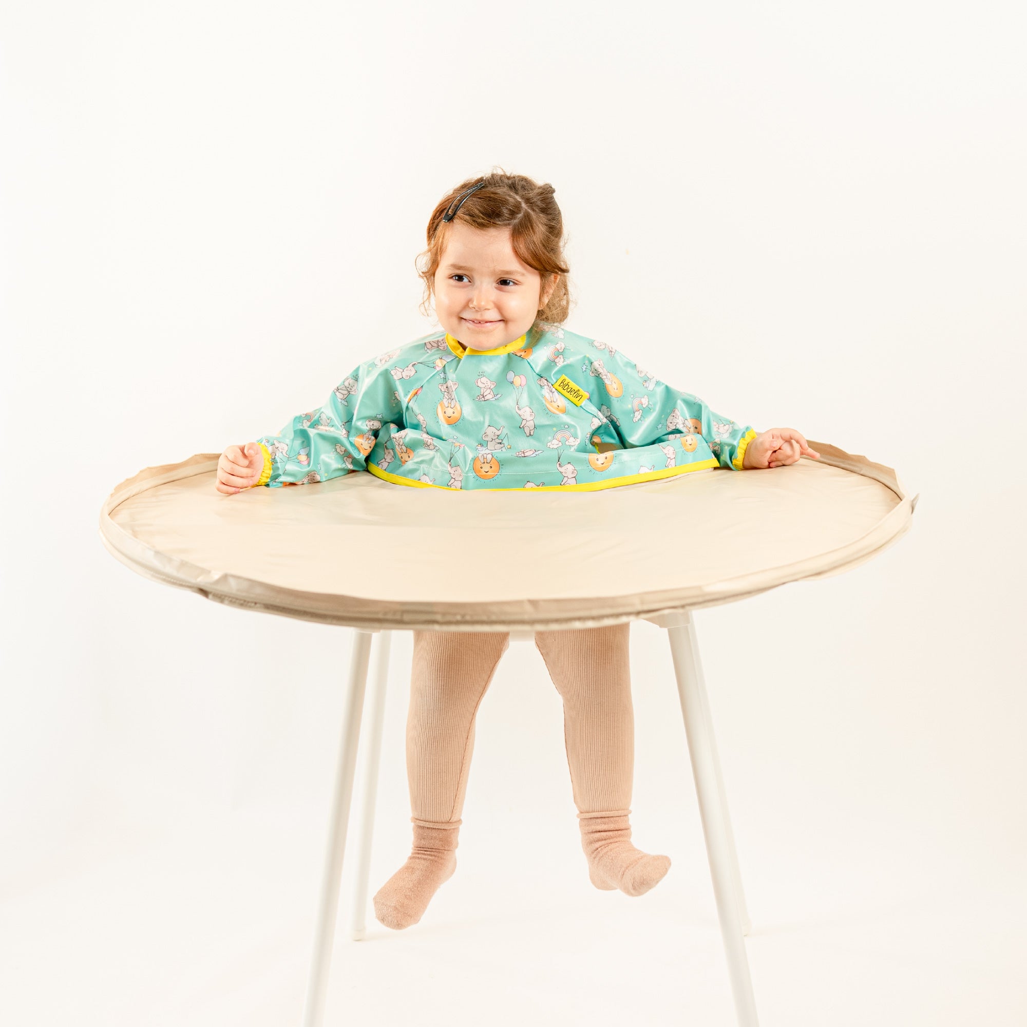 Bavoir de rechange bleu-vert à motifs pour kits BibaTray M et L, vue complète sur bébé. | Replacement blue-green patterned bib for BibaTray M and L kits, full view on baby.