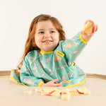 Bébé mangeant des morceaux de pomme en toute autonomie avec le bavoir bleu-vert Bibaelin. | Baby self-feeding apple pieces with the teal Bibaelin bib.