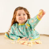 Bébé mangeant des morceaux de pomme en toute autonomie avec le bavoir bleu-vert Bibaelin. | Baby self-feeding apple pieces with the teal Bibaelin bib.