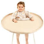 Enfant souriant utilisant le grand kit bavoir plateau intégral Bibatray-L beige | Smiling child using the large beige Bibatray-L full bib tray kit.