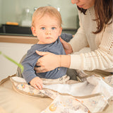 Maman installant le bavoir plateau Bibatray-M sur un bébé en chaise haute - Mother setting up the Bibatray-M bib tray on a baby.