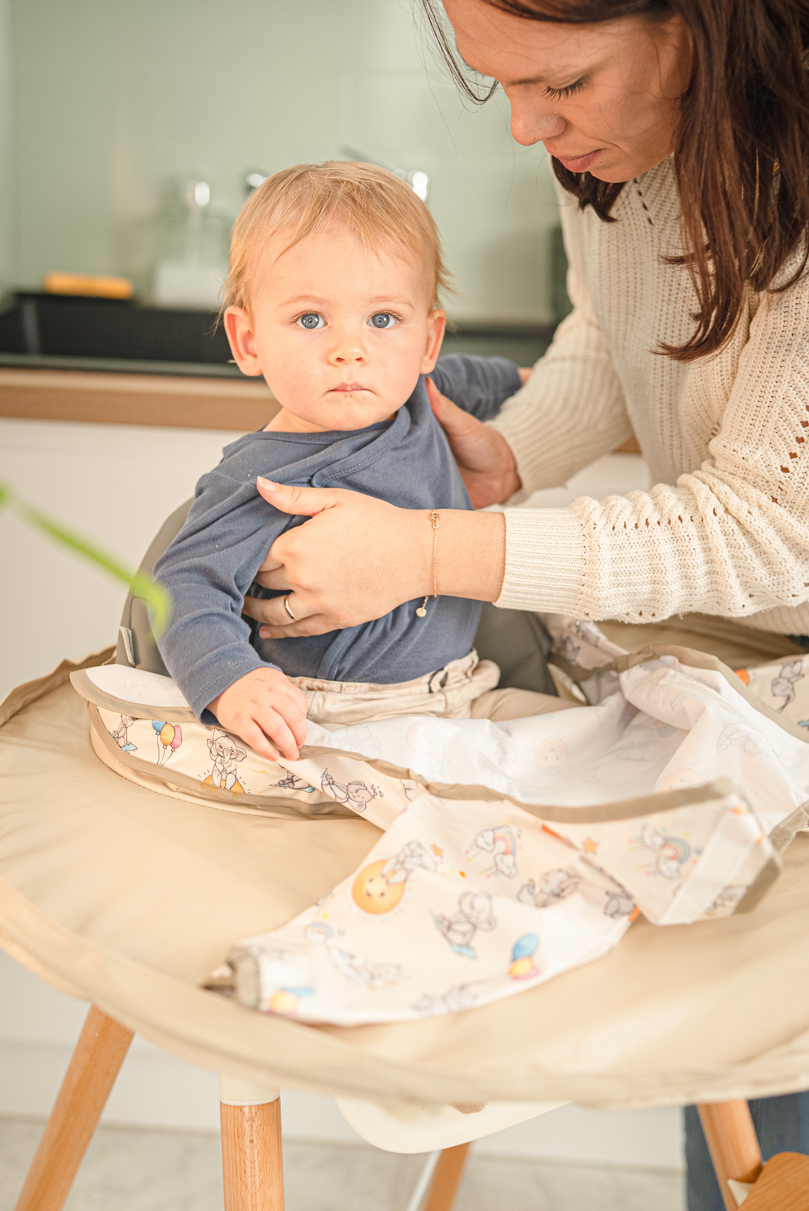 Maman installant le bavoir plateau intégral Bibaelin sur un bébé en chaise haute pour un repas propre - Mother setting up the Bibaelin bib tray on a baby.