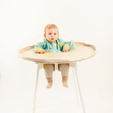 Bavoir de rechange bleu-vert à motifs pour kits BibaTray M et L, vue complète sur bébé. | Replacement blue-green patterned bib for BibaTray M and L kits, full view on baby.