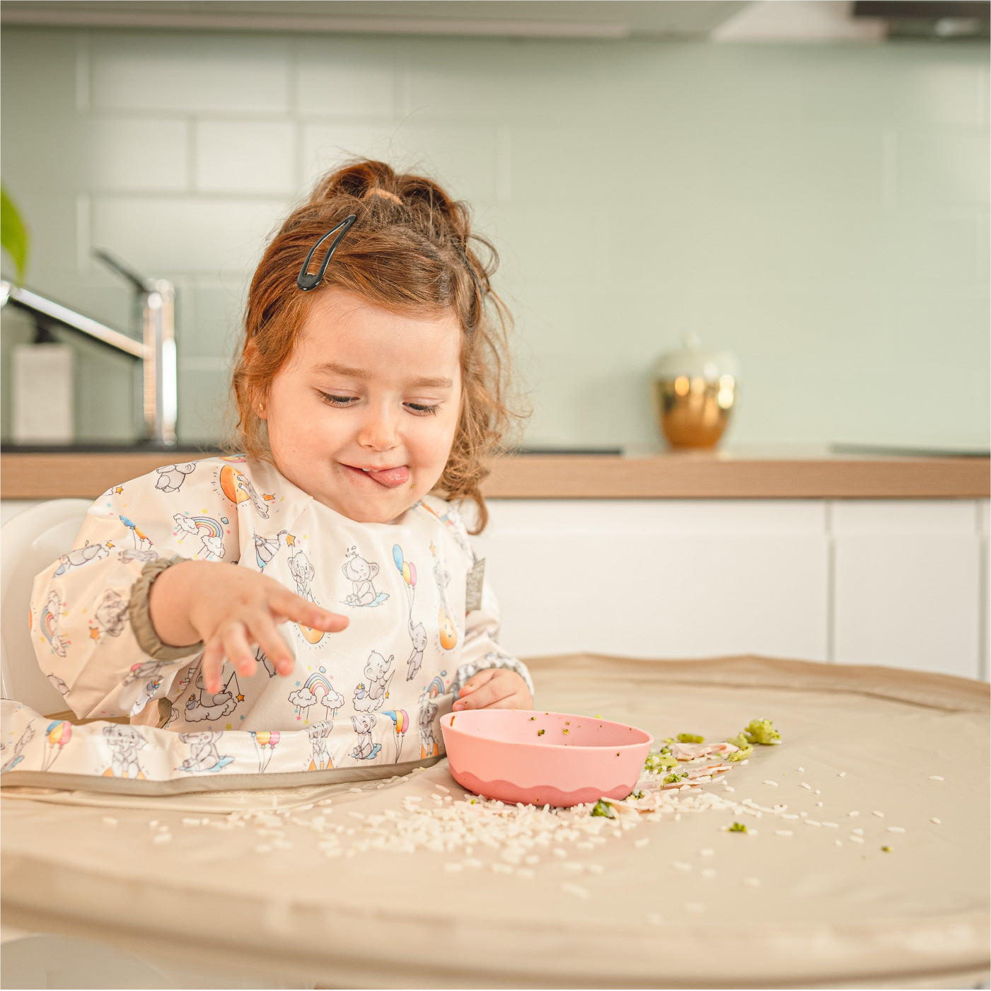 Toddler sitting at a Bibatray weaning station with a messy pink bowl. | Jeune enfant assis à une station de sevrage Bibatray avec un bol rose et des restes de nourriture.