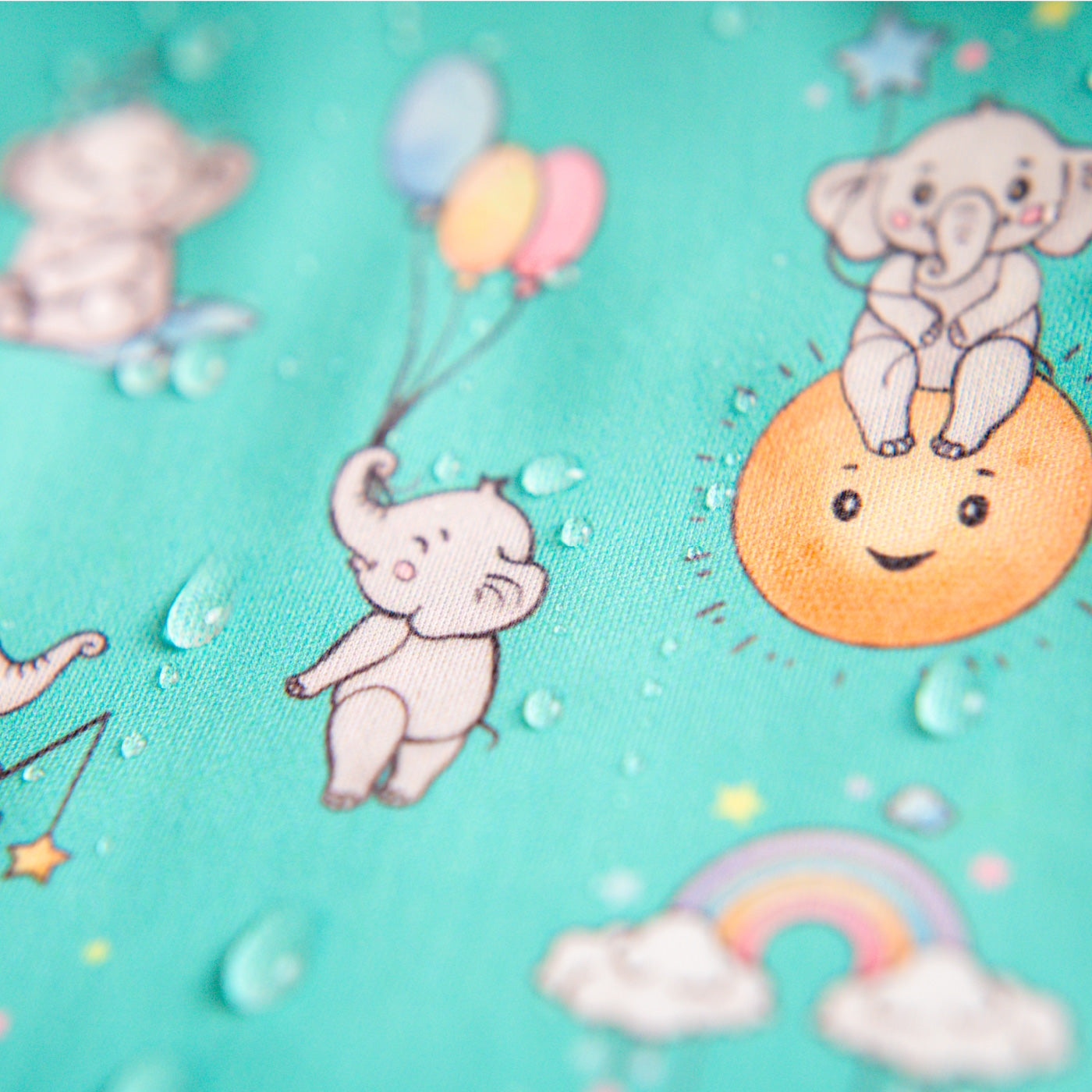 Macro shot of waterproof bib fabric with water droplets and elephant patterns. | Prise de vue macro du tissu imperméable du bavoir avec gouttes d'eau et motifs éléphants.